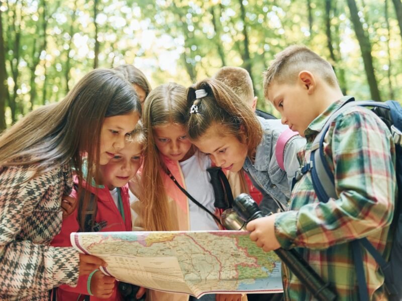 Using map. Kids in green forest at summer daytime together