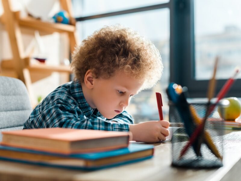 selective focus of curly kid writing near books